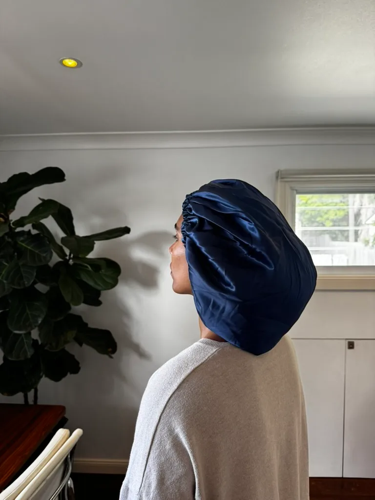 Side profile of a person wearing a navy silk bonnet indoors beside a plant.