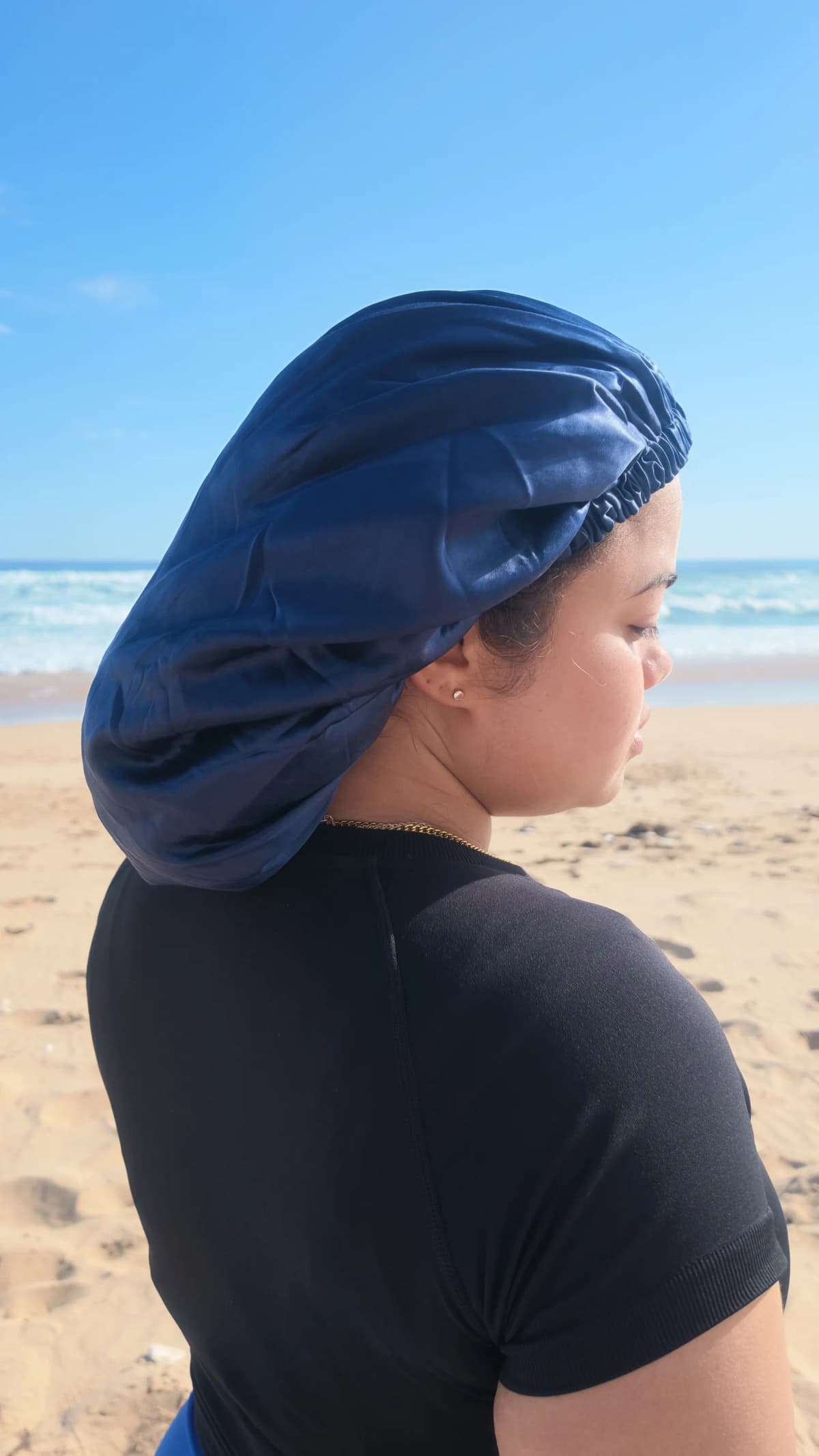 Back view of a person wearing a long navy silk bonnet at the beach.