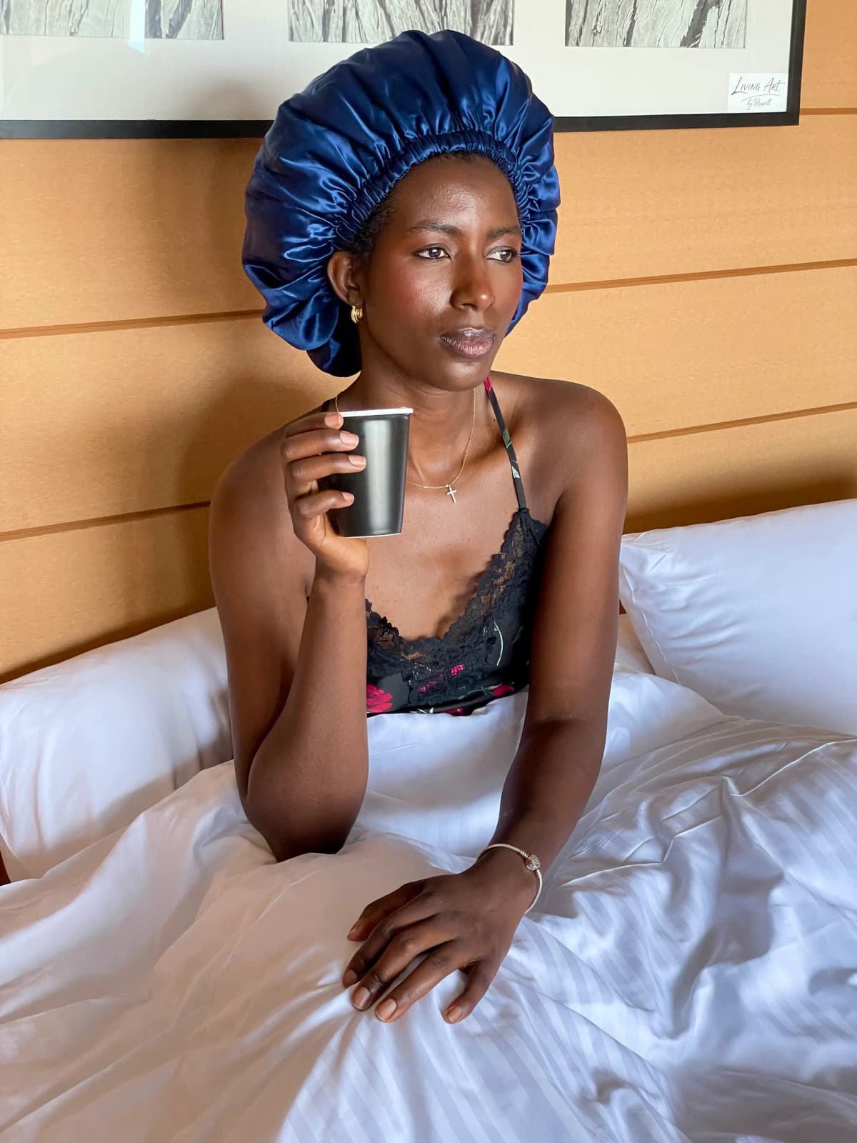 Person wearing a navy silk bonnet, sitting in bed holding a mug.