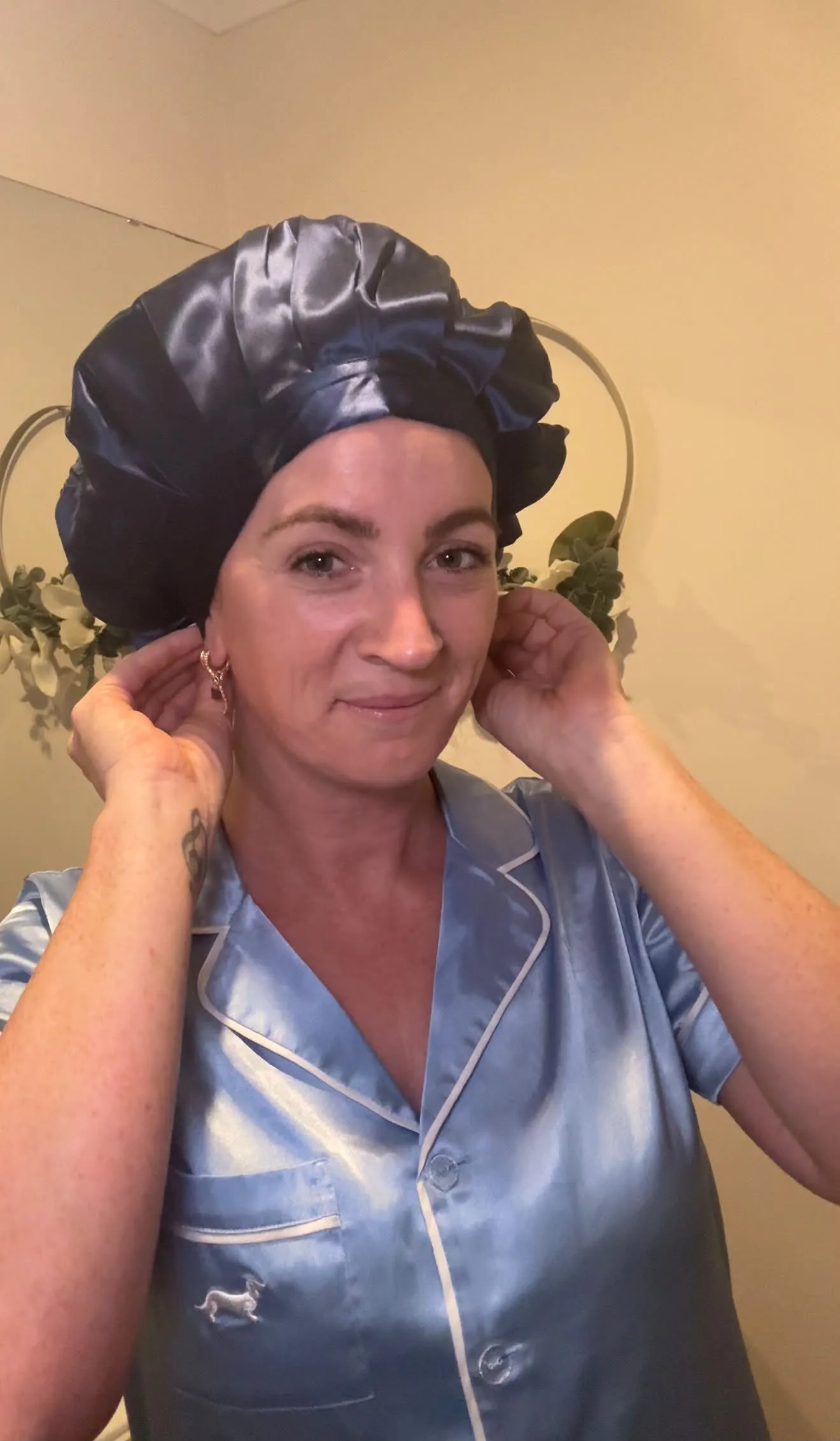 Customer adjusting the navy Kova Silk All Rounder bonnet while wearing blue satin pyjamas.