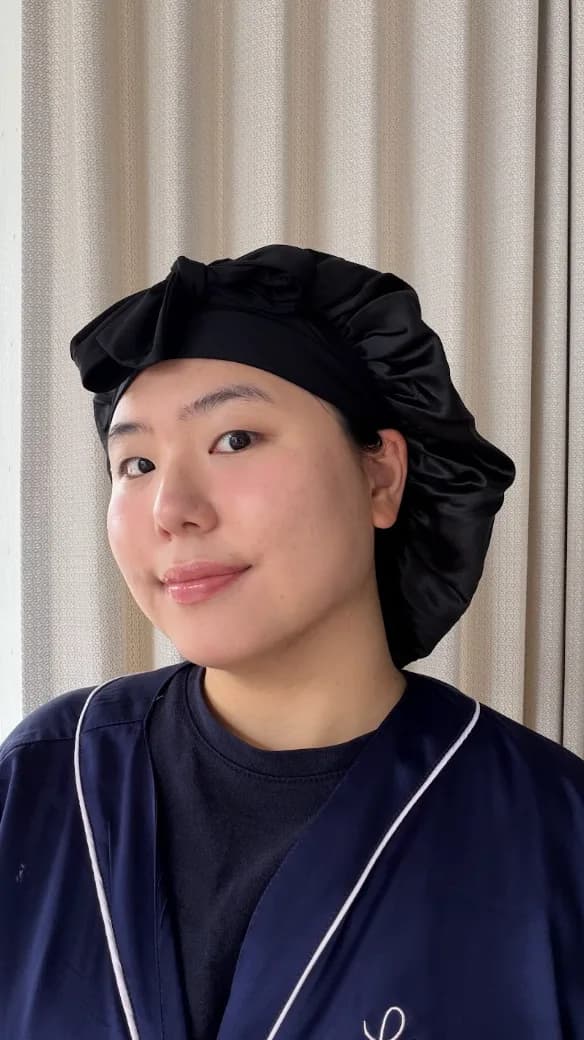Front view of a person wearing a black silk bonnet and a navy robe, in front of a curtain.