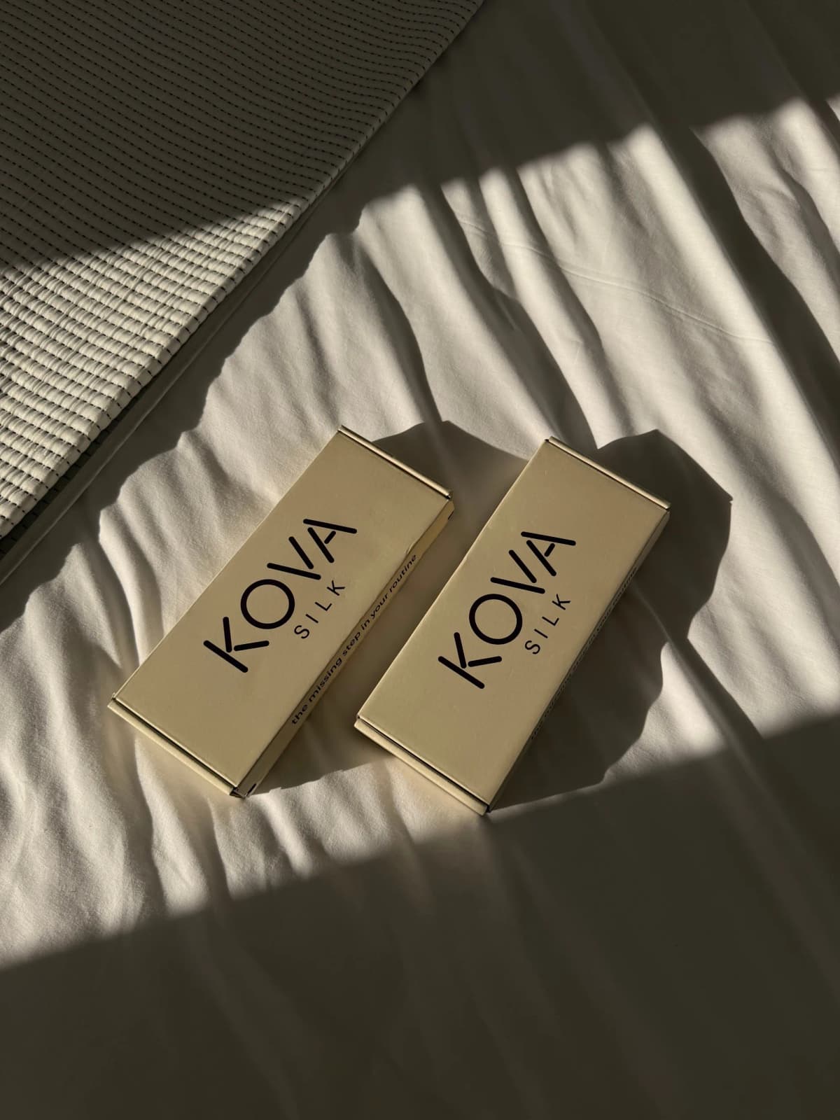 Two closed Kova Silk boxes resting on sunlit bed linen