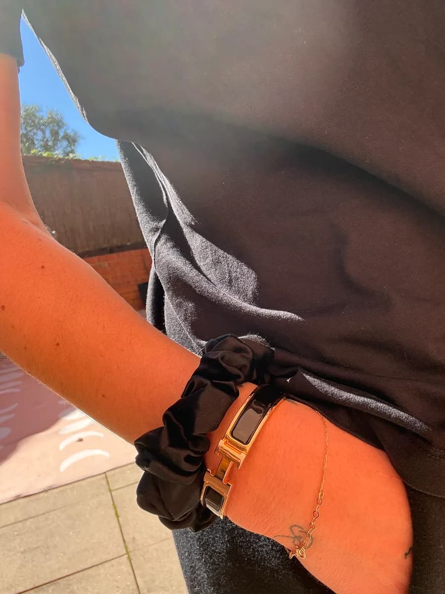Close-up of a wrist wearing a black Kova Silk scrunchie beside a rose-gold watch and gold chain